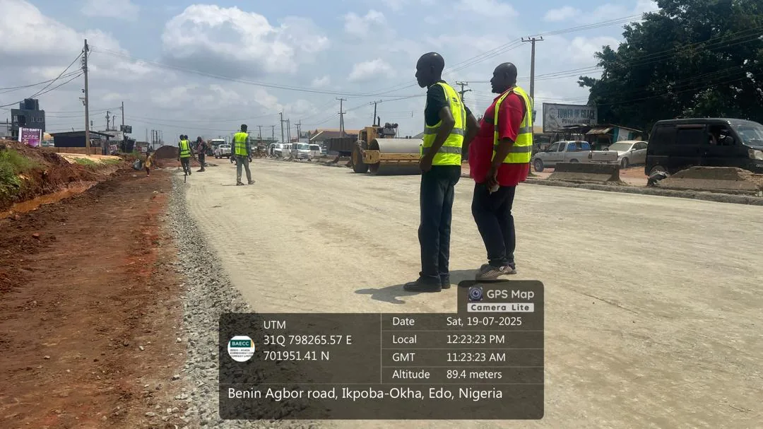 Compacted base course on a completed section of the Benin-Agbor road at Ikpoba-Okha, Edo State, with site staff in high-visibility vests.